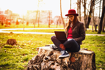 junge Frau sitzt in der Natur vor Laptop